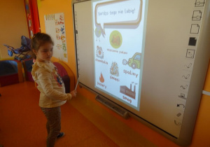 Dziewczynka stoi pod tablicą interaktywną ze wskaźnikiem.